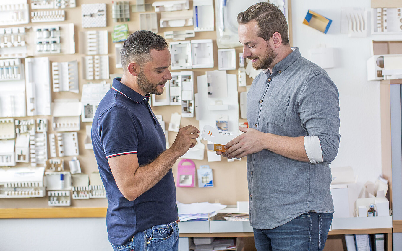 Entwicklung innovativer Kombiprodukte bei Faller Packaging: Zwei Experten begutachten eine pharmazeutische Faltschachtel mit integriertem Beipackzettel